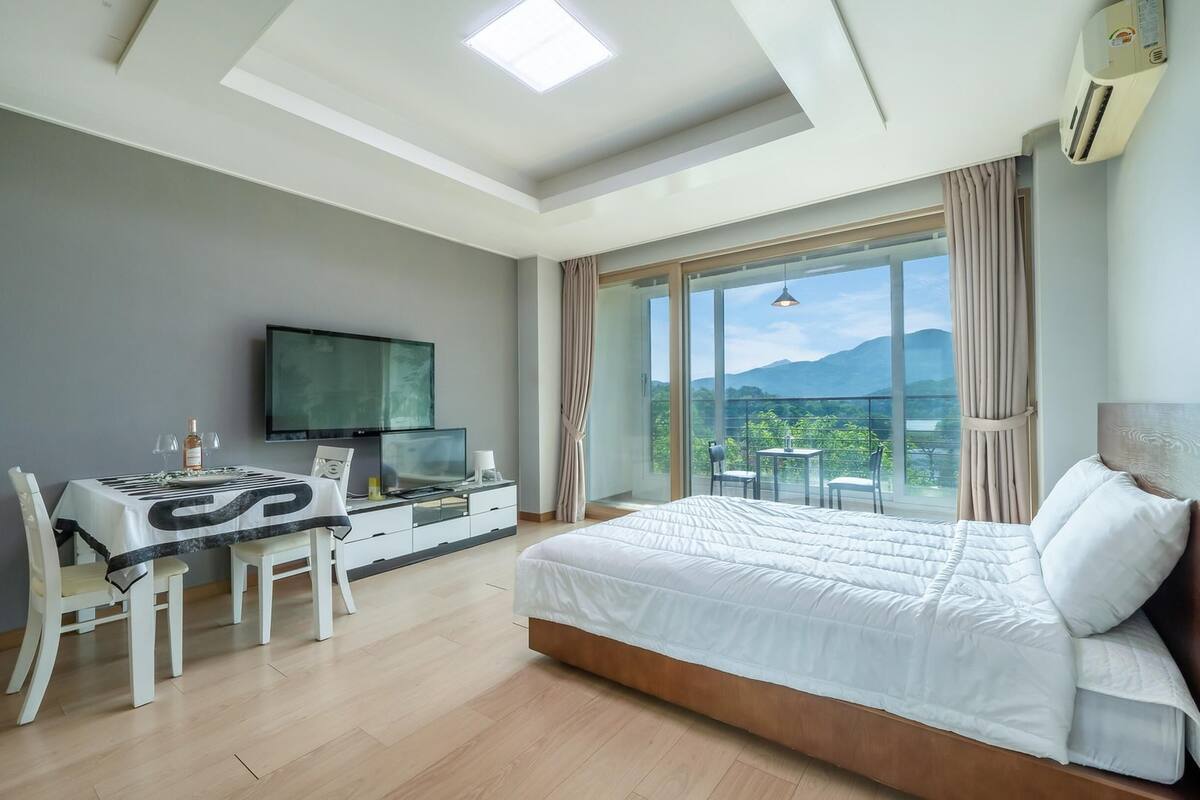 A modern hotel room with a large bed, a dining table, and a TV.