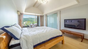 A bedroom with a large bed, a TV mounted on the wall, and a balcony with a view of the countryside. - Gapyeong Yeonkkocchosu Pet Pension (Gapyeong)