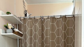 Ein Badezimmer mit einem Duschvorhang mit sechseckigem Muster, einer weißen Toilette, einem мраморном Waschbecken und einem Regal mit Pflanzen und einer kleinen Vase.