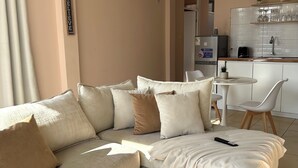 Ein modernes Wohnzimmer mit einer Eckcouch, einem flauschigen Teppich, einer Küchenzeile mit Spüle und Schränken sowie einer Deckenleuchte.