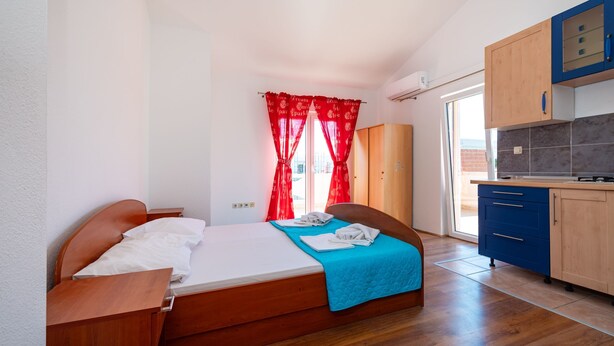A bedroom with a bed, a small desk, a wardrobe, and a kitchen area with cabinets and a countertop. - Bonvie Apartments in Center B3 (Novalja)