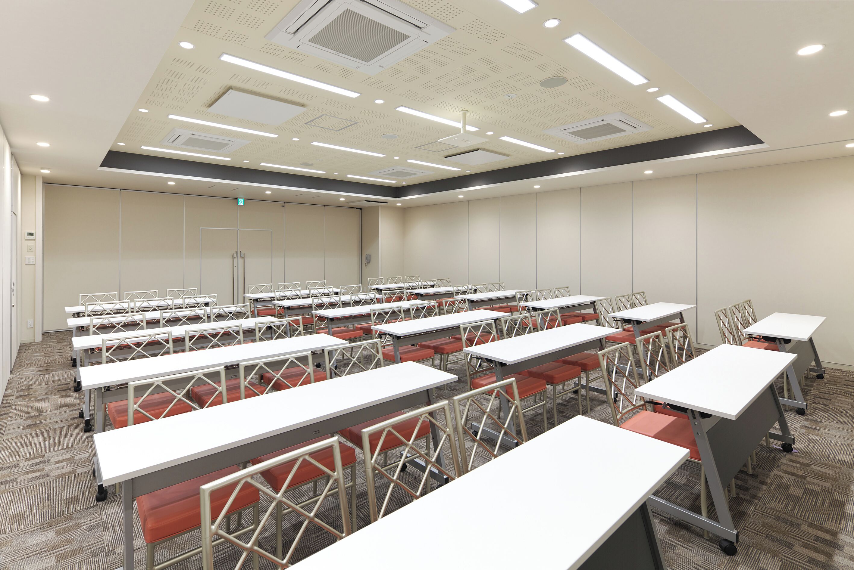 A conference room with multiple tables and chairs, equipped with ceiling lights and ventilation.