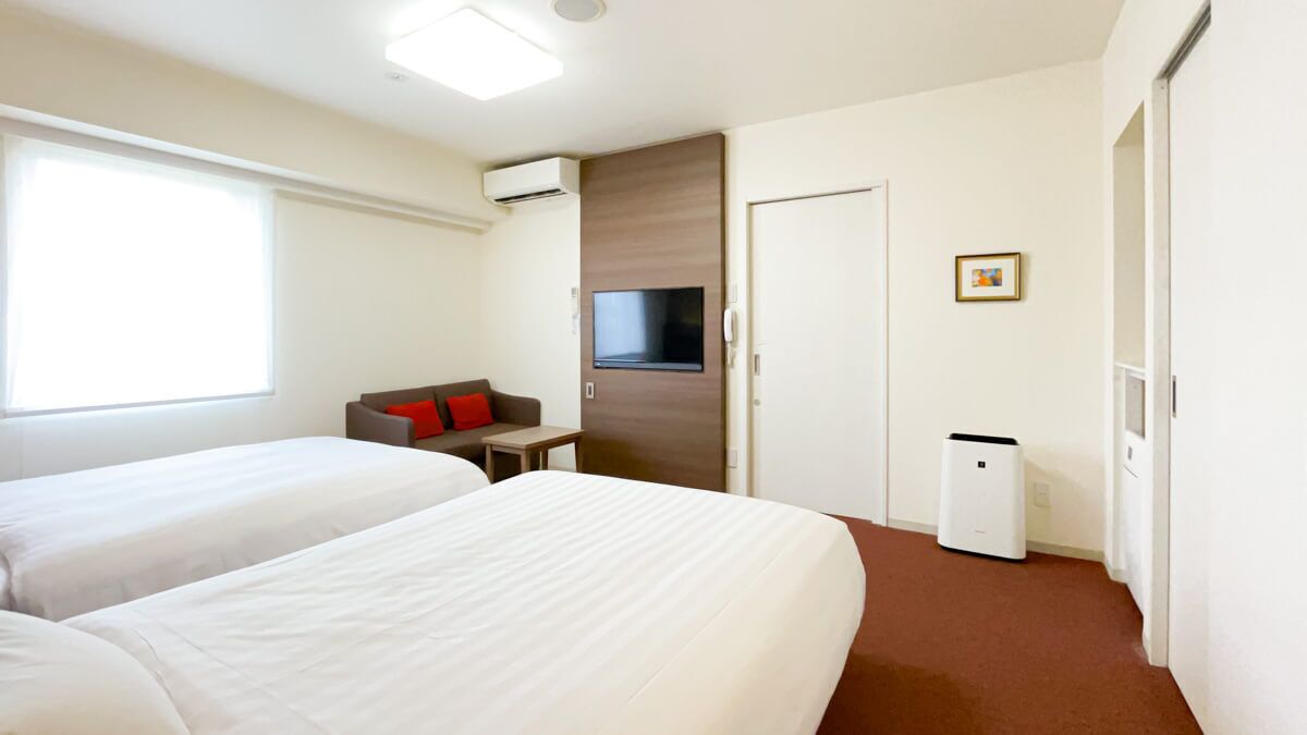 Habitación de hotel con dos camas, un escritorio, un televisor y un armario.