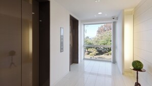 A modern hallway with a large window, an elevator, and a small table with a plant. - Hotel Green Core Bando (Bando)