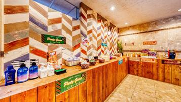 Un área de recepción con un mostrador de madera, diferentes alimentos y bebidas, y señales que indican servicios como un juego para fiestas.