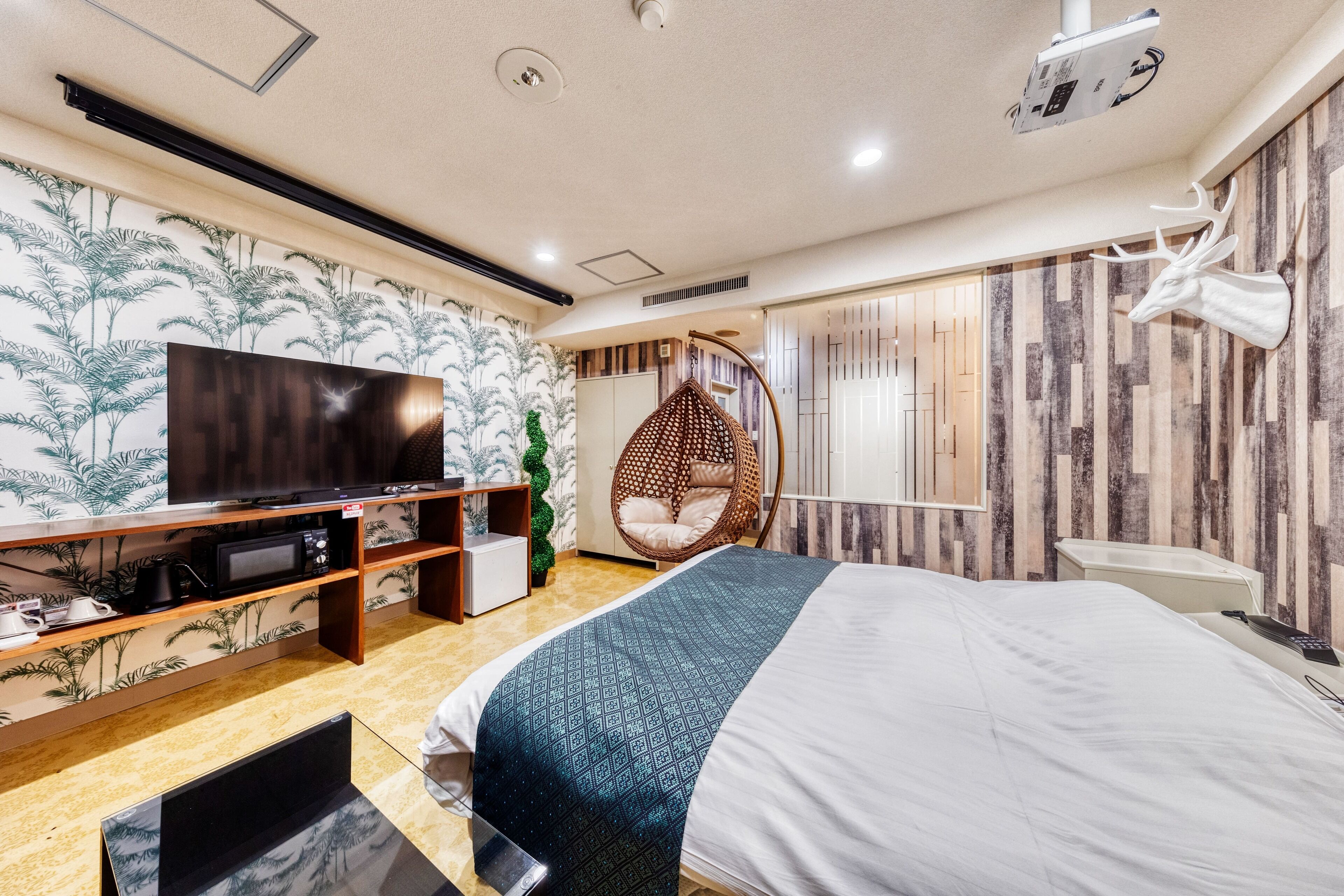 A modern hotel room with a large bed, a television, a wooden shelf, and a decorative wall.
