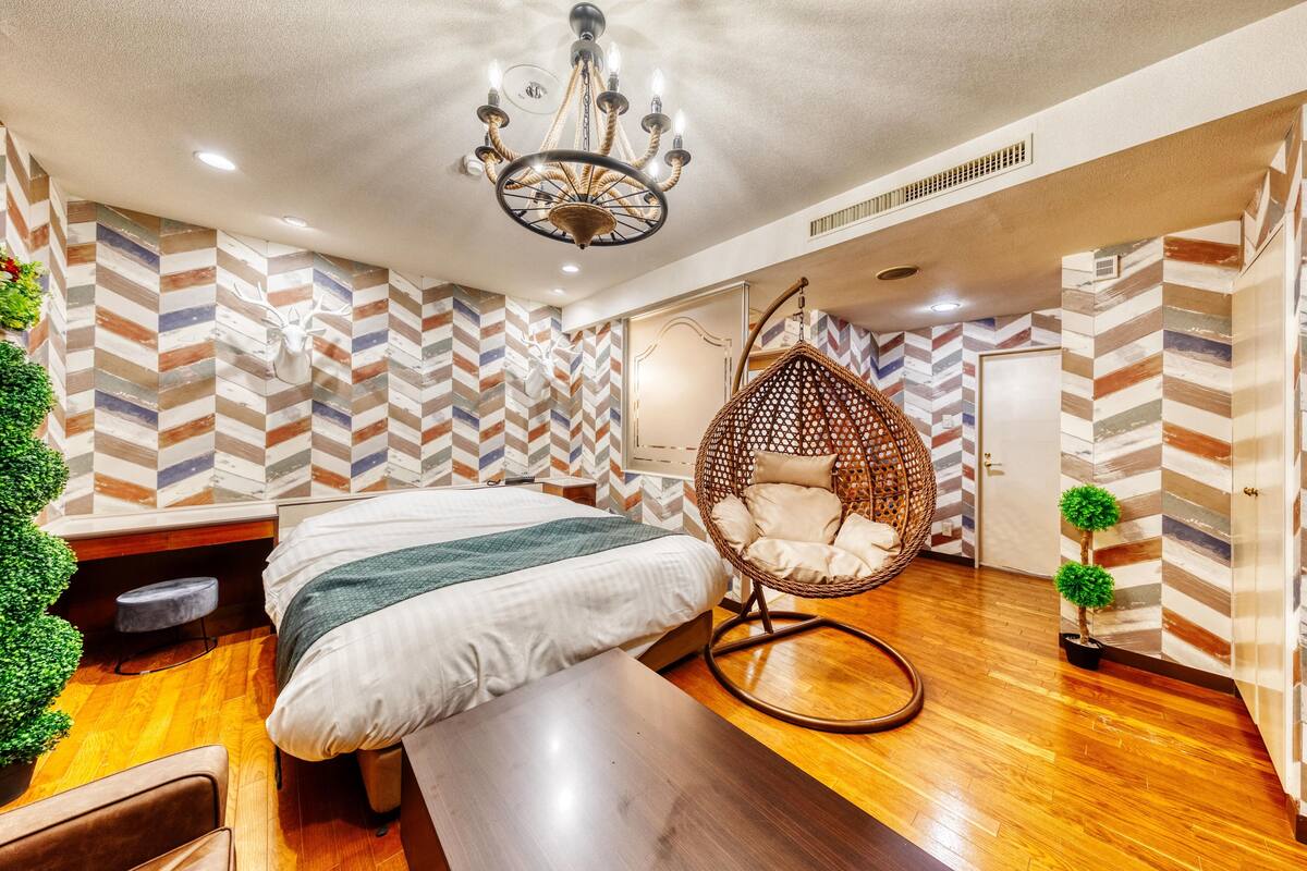 A modern hotel room with a bed, a hanging chair, a bench, and a potted plant.