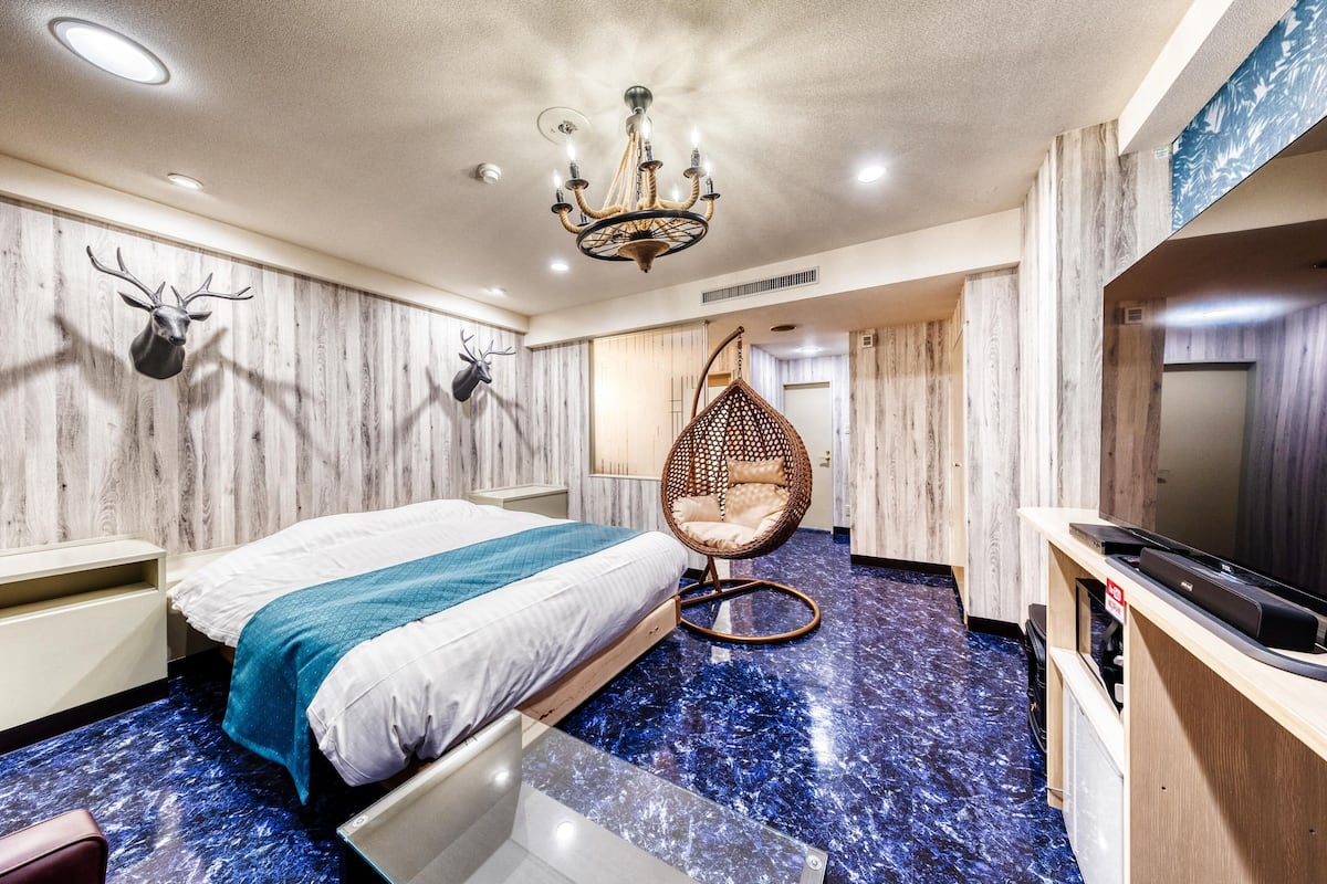 A modern bedroom with a bed, a hanging chair, a TV, and a wooden wall with antlers.
