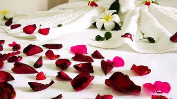 A bed with a white bedspread, a white towel, and scattered rose petals.