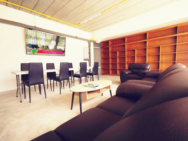 A modern lounge area with a sofa, chairs, a coffee table, and a TV screen. - BBVC Hostel Collegestay (Koh Samui)