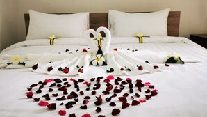 Una cama impecable con sábanas blancas, un arreglo de pétalos de rosa en forma de corazón y flores decorativas.