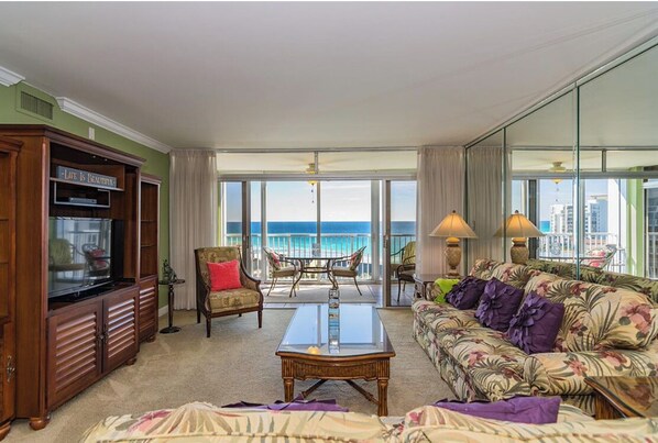 A spacious living room with a large window overlooking the ocean, a television, and a sofa with floral upholstery. - Beachside Bungalow (Destin)