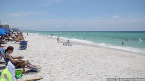 Ein Strand mit Menschen, die sonnenbaden und schwimmen, Sonnenschirmen und Liegestühlen.