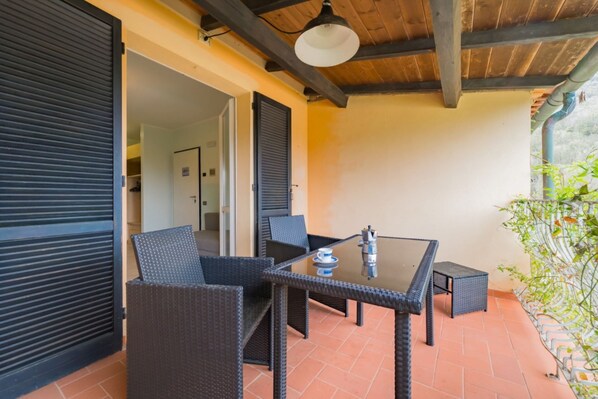 An outdoor patio with wicker furniture, a glass table, and a coffee maker.