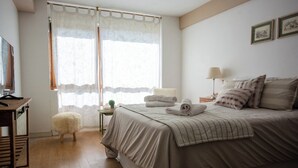 Ein Schlafzimmer mit Bett, Schreibtisch, Lampe und einem Fenster mit Vorhängen.