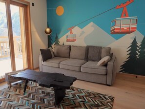 A living room with a sofa, a coffee table, and a mural of a mountain scene with a cable car. - Paradiski new, calm and sunny Plan peisey (PEISEY-NANCROIX)