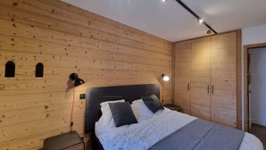 Ein Schlafzimmer mit Holzwand, einem Bett mit Kissen, einem Nachttisch, einer Lampe und einem Kleiderschrank.