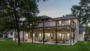Ein modernes, zweistöckiges Haus mit überdachter Terrasse, großen Fenstern und einem gepflegten Rasen.