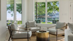 Ein modernes Wohnzimmer mit großen Fenstern, grauen Polsterstühlen und einem runden Couchtisch.