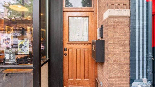 Una puerta de madera con un panel de vidrio, un buzón pequeño y un muro de ladrillo.