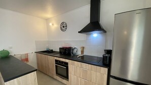 A modern kitchen with a stainless steel refrigerator, a black range hood, a built-in oven, and a black countertop. - Le Clos de l'Allamanda - Le Marin (LE MARIN)