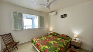 A bedroom with a bed, a chair, a nightstand, a window, and a ceiling fan. - Le Clos de l'Allamanda - Le Marin (LE MARIN)