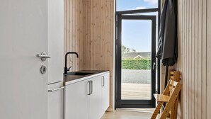 Een compacte keuken met een zwarte kraan, witte kasten en een houten inrichting. Een schuifdeur van glas leidt naar een buitenruimte met een houten terras en een haag.