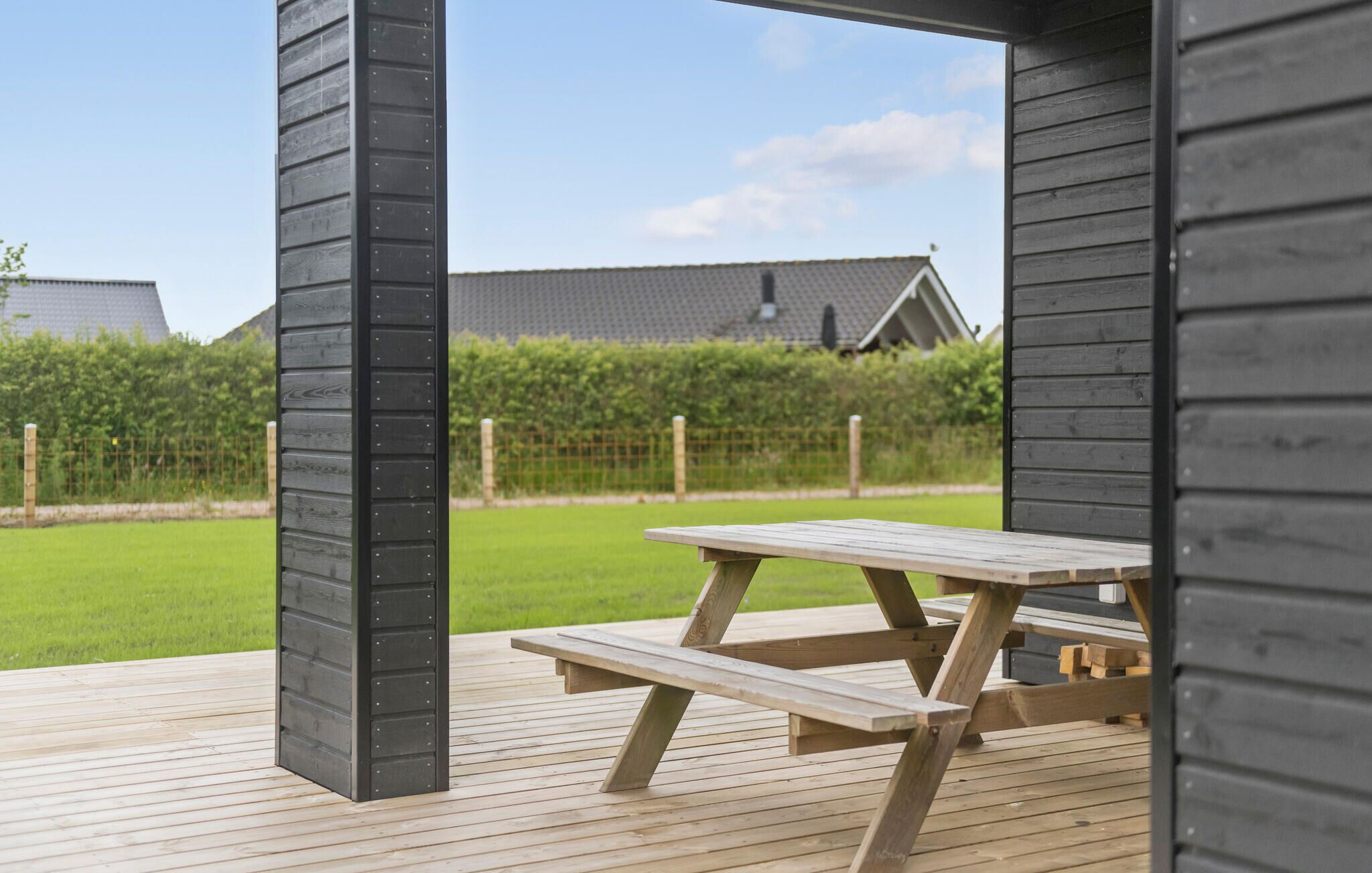 Une terrasse en bois à l’extérieur, avec une table de pique-nique, entourée d’une clôture et de verdure.
