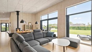 Een moderne woonkamer met een hoekbank, een ronde salontafel en grote ramen met uitzicht op de omgeving.