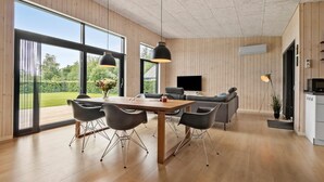 Een moderne woonkamer met een eethoek, grote ramen, een flatscreen televisie en een keuken.