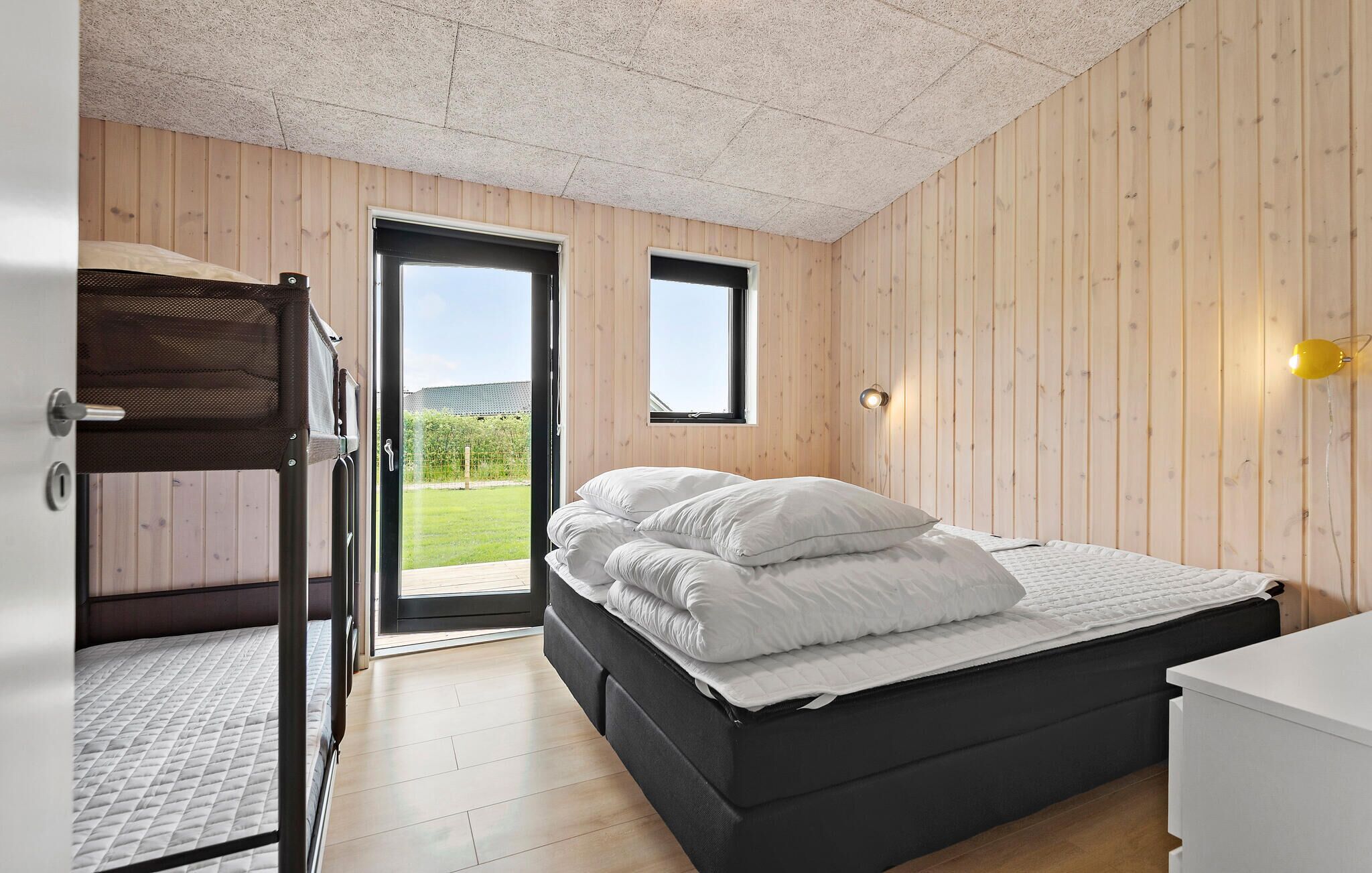 A bedroom with a bunk bed, a single bed, a small window, and a door leading to an outdoor area.