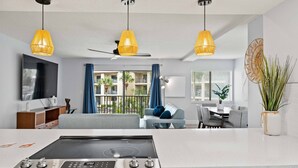 Eine moderne Küche mit Einbauherd, eine Essecke mit Tisch und Stühlen sowie ein Wohnzimmer mit Sofa und Fernseher.