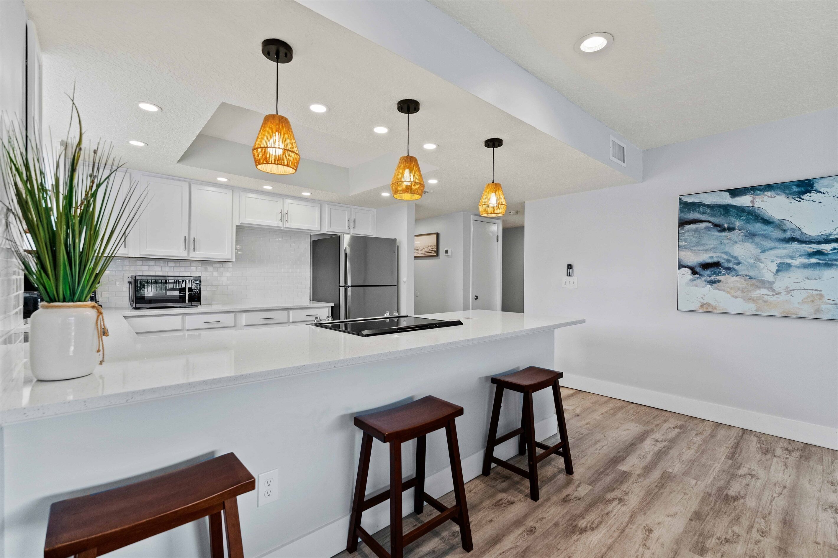 Una cucina moderna con mobili bianchi, un'isola centrale con sgabelli, illuminazione a sospensione e un grande quadro astratto appeso al muro.