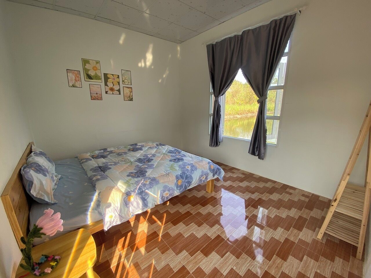 A bedroom with a bed, a window with curtains, a wooden ladder, and a herringbone-patterned floor.