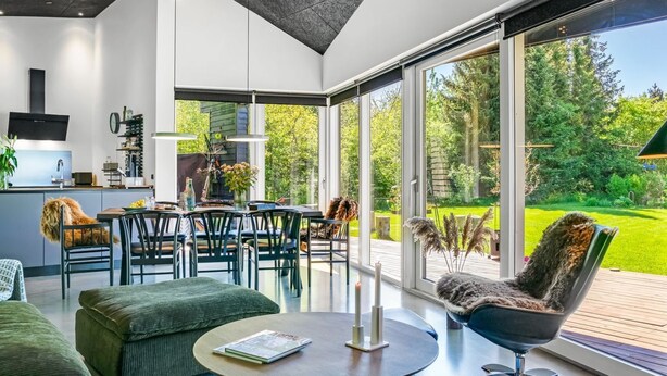 A modern kitchen with a built-in oven, a dining area with a table and chairs, and a large sliding glass door leading to a deck with a view of a green landscape. - "Melina" - 900m to the fjord by Interhome (Farsø)