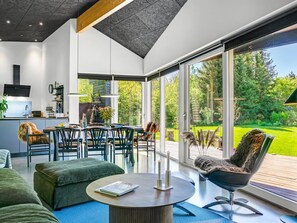 A modern kitchen with a built-in oven, a dining area with a table and chairs, and a large sliding glass door leading to a deck with a view of a green landscape.