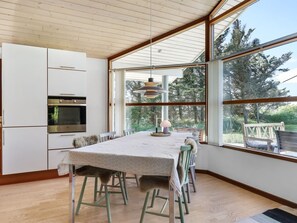 Une cuisine moderne dotée d’appareils électroménagers intégrés, un coin repas avec une table et des chaises, et de grandes fenêtres offrant une vue sur l’extérieur.