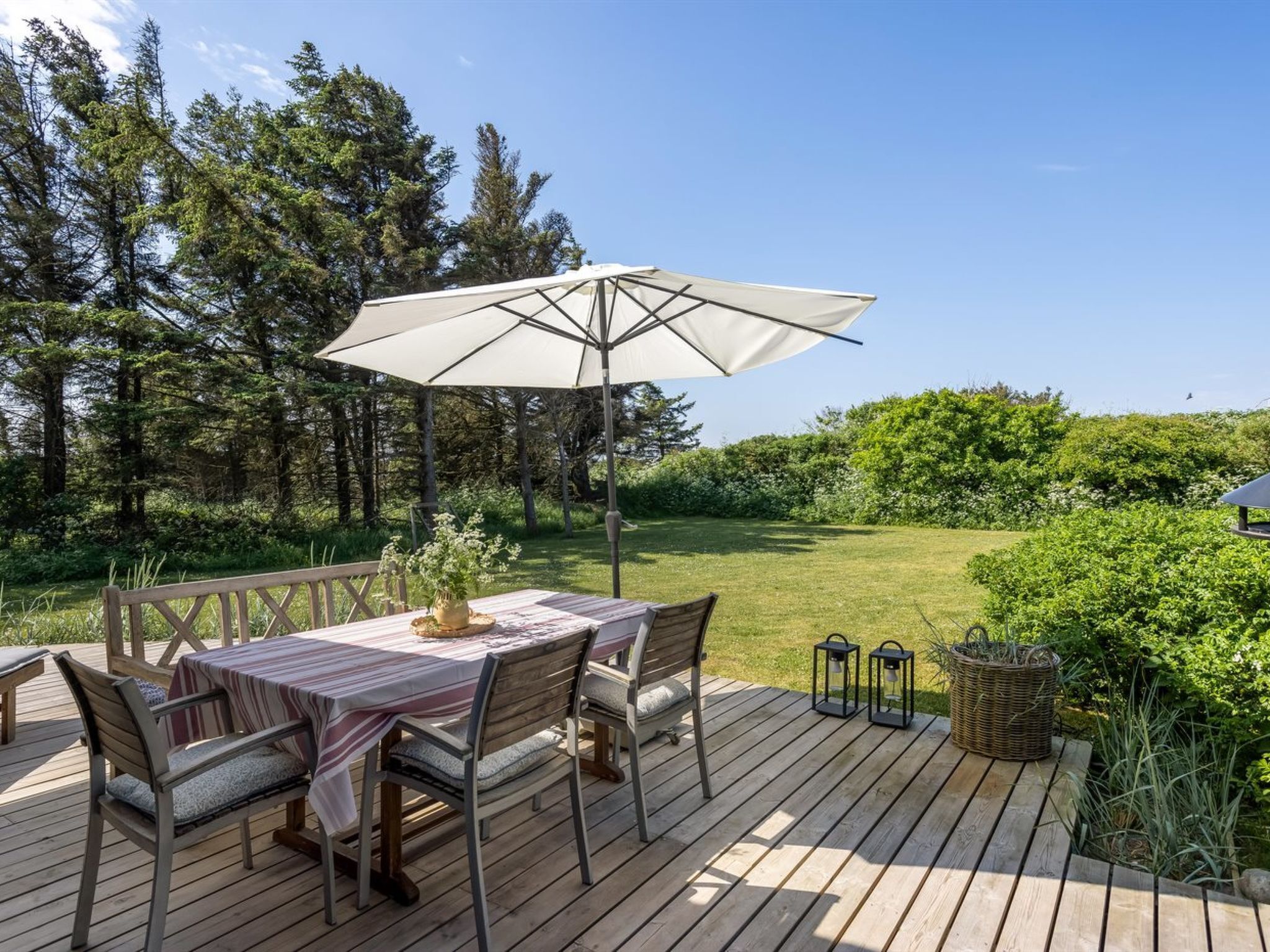 Een terras buiten met een tafel en stoelen, omringd door begroeiing en bomen.