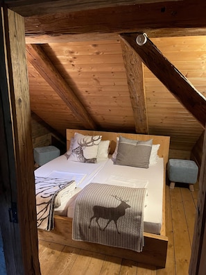 A cozy loft bedroom with a wooden ceiling, a bed with patterned bedding, and two matching ottomans.