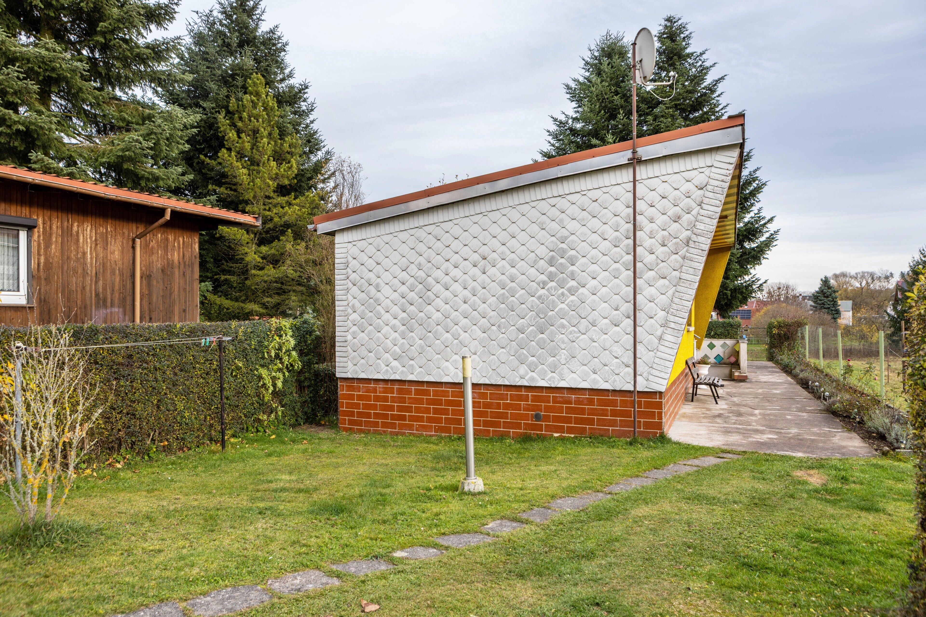 Une maison dont la façade se distingue par son aspect particulier, avec une base en briques et un petit jardin agrémenté d’un sentier.
