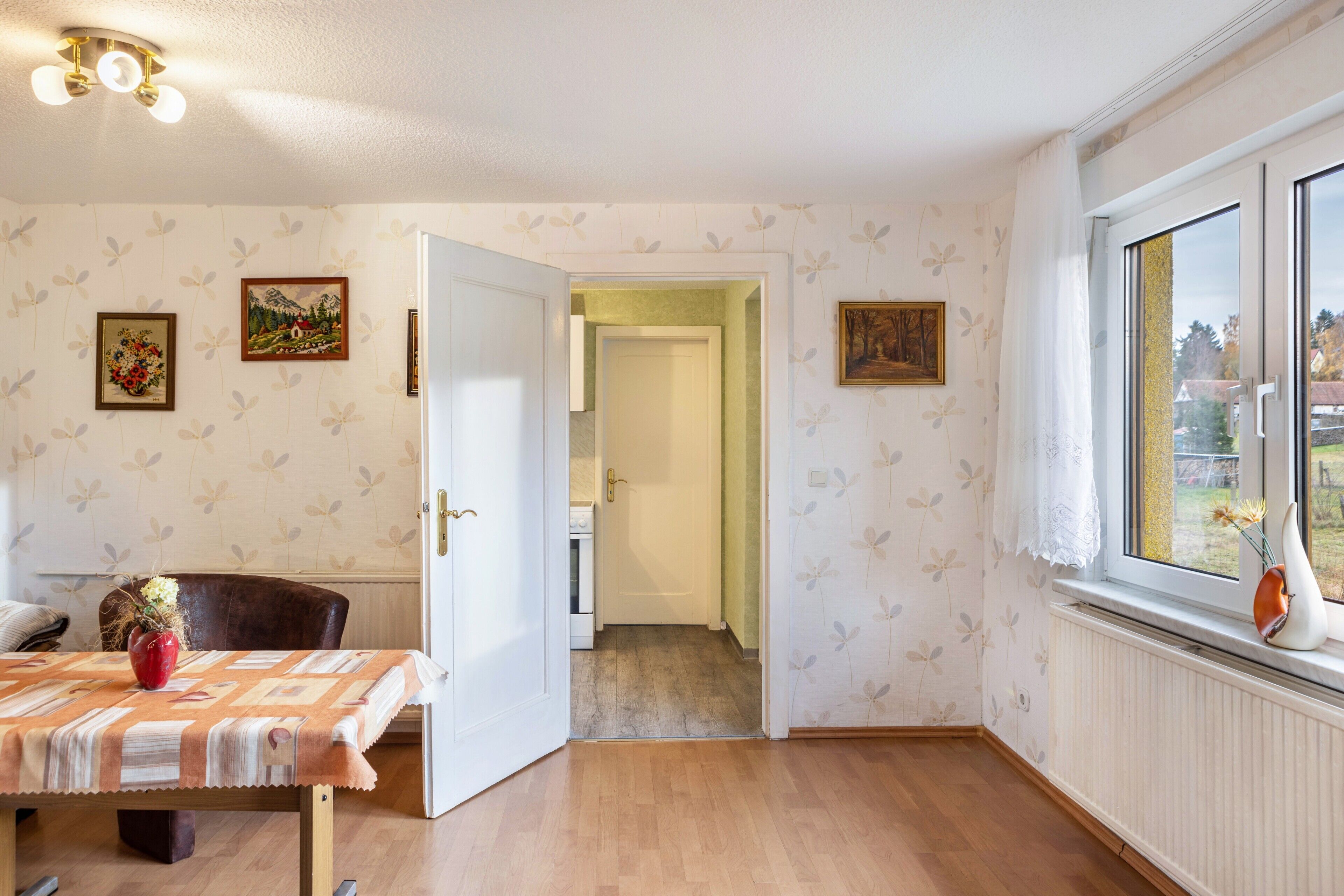 Ein Zimmer mit Esstisch, Stuhl, einer zur Diele führenden Tür und einem Fenster mit Blick.