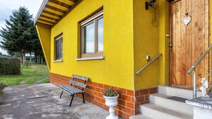 Un edificio amarillo con puerta de madera, un banco y una planta en maceta.