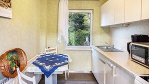 Una cocina compacta con ventana, armarios blancos, microondas y lavamanos.