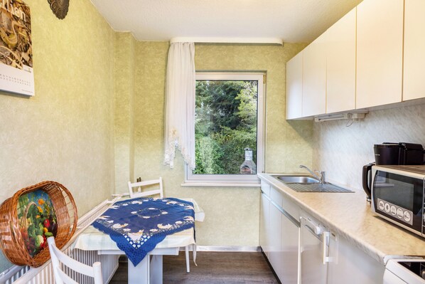 Una cocina compacta con ventana, armarios blancos, microondas y lavamanos.