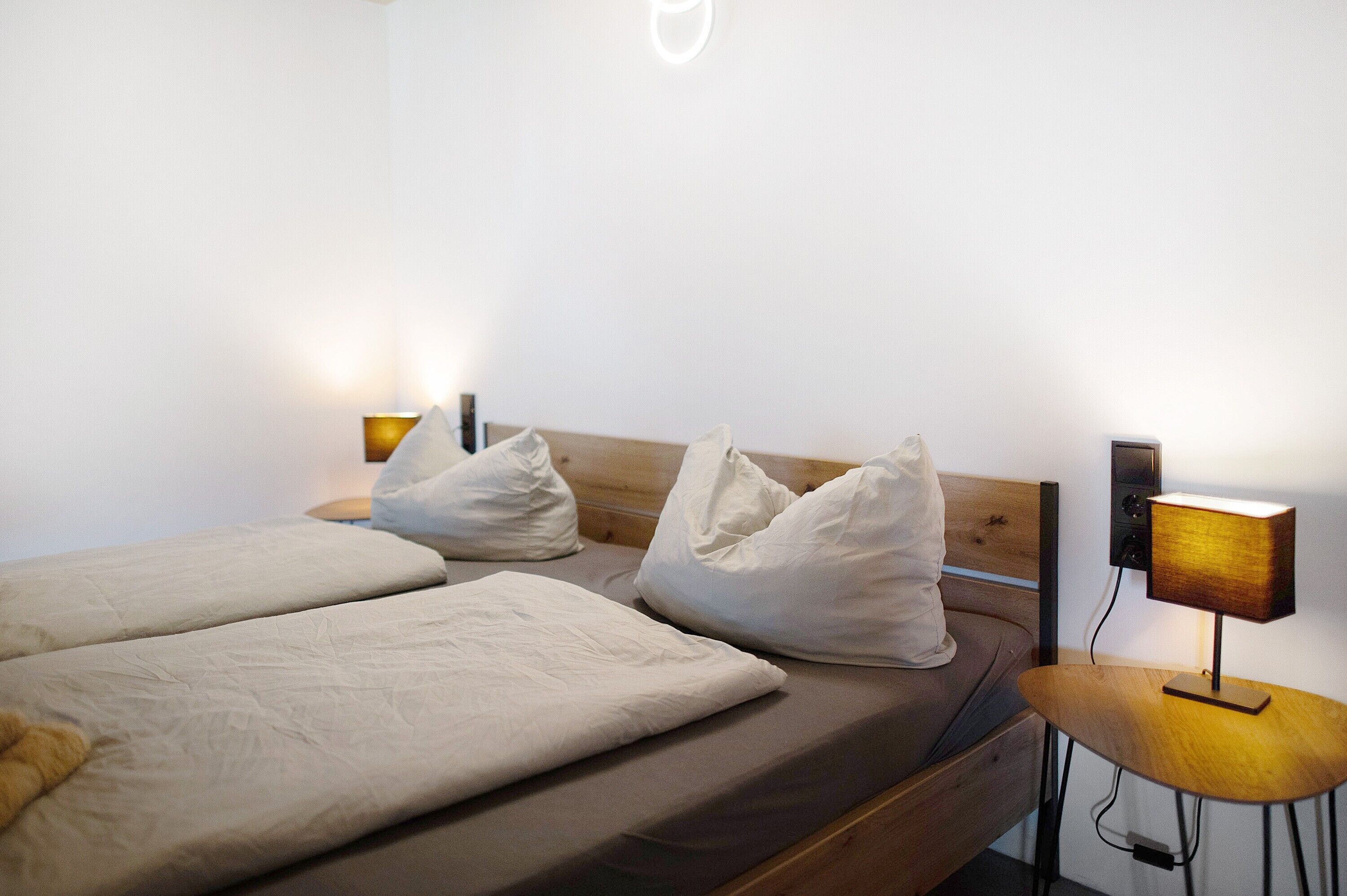 A double bed with white bedding, a bedside table with a lamp, and a wall-mounted light fixture.