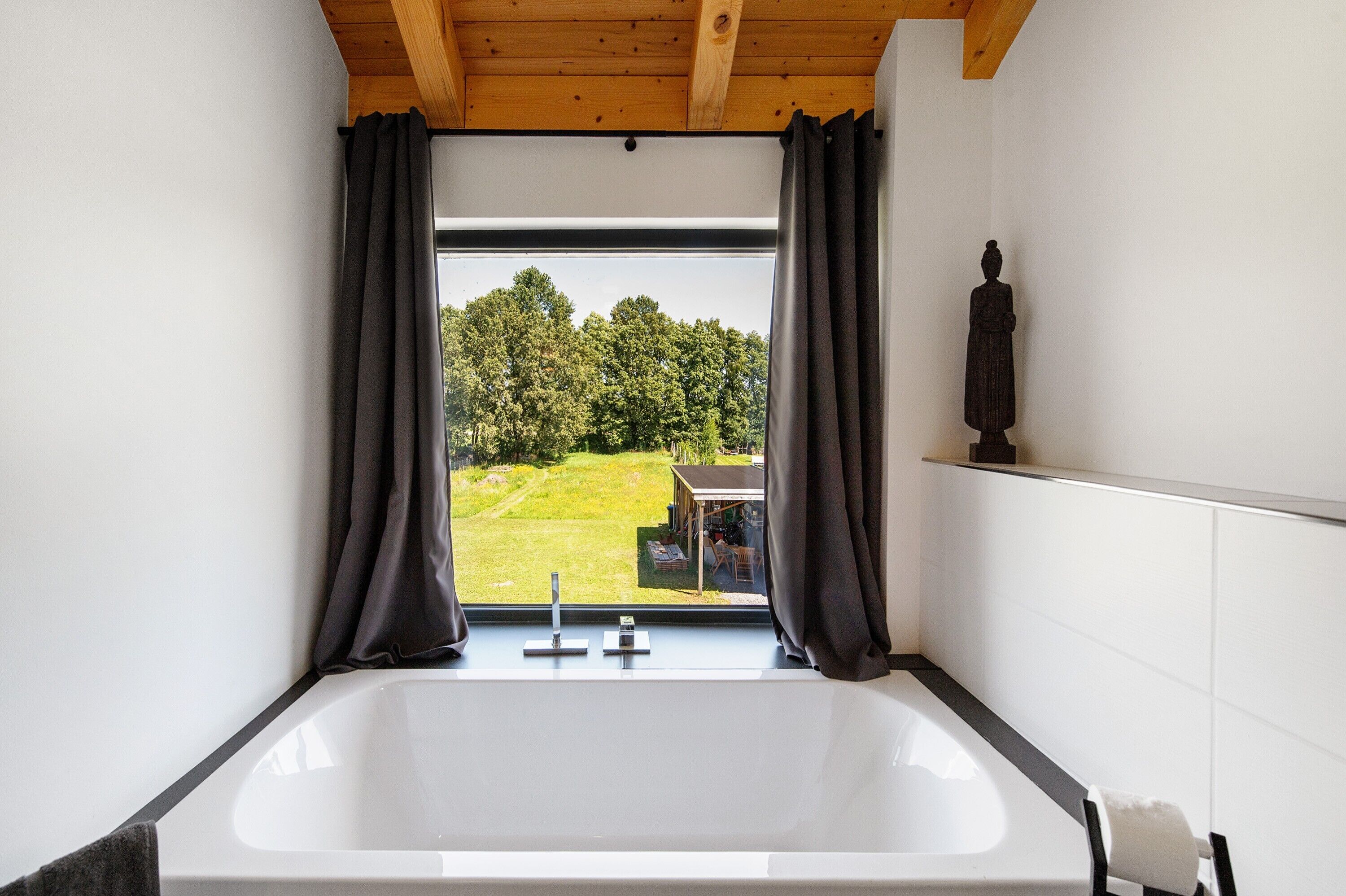 Un baño con una bañera grande, vigas de techo de madera y vistas a un paisaje verde.