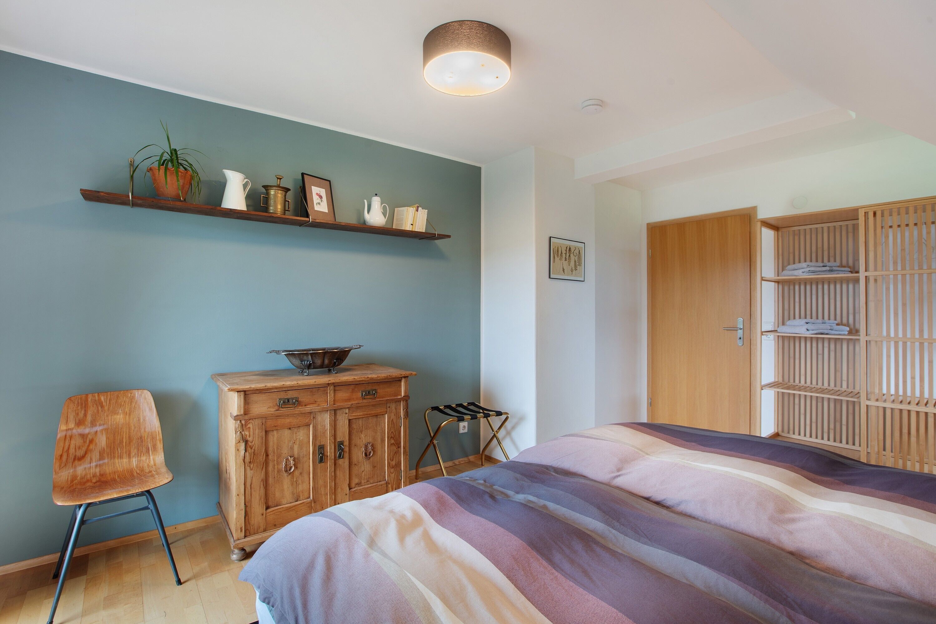 A bedroom with a bed, wooden dresser, shelves, and a chair.