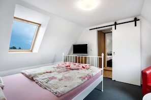 A bedroom with a bed, a TV, a window, and a door leading to a bathroom.