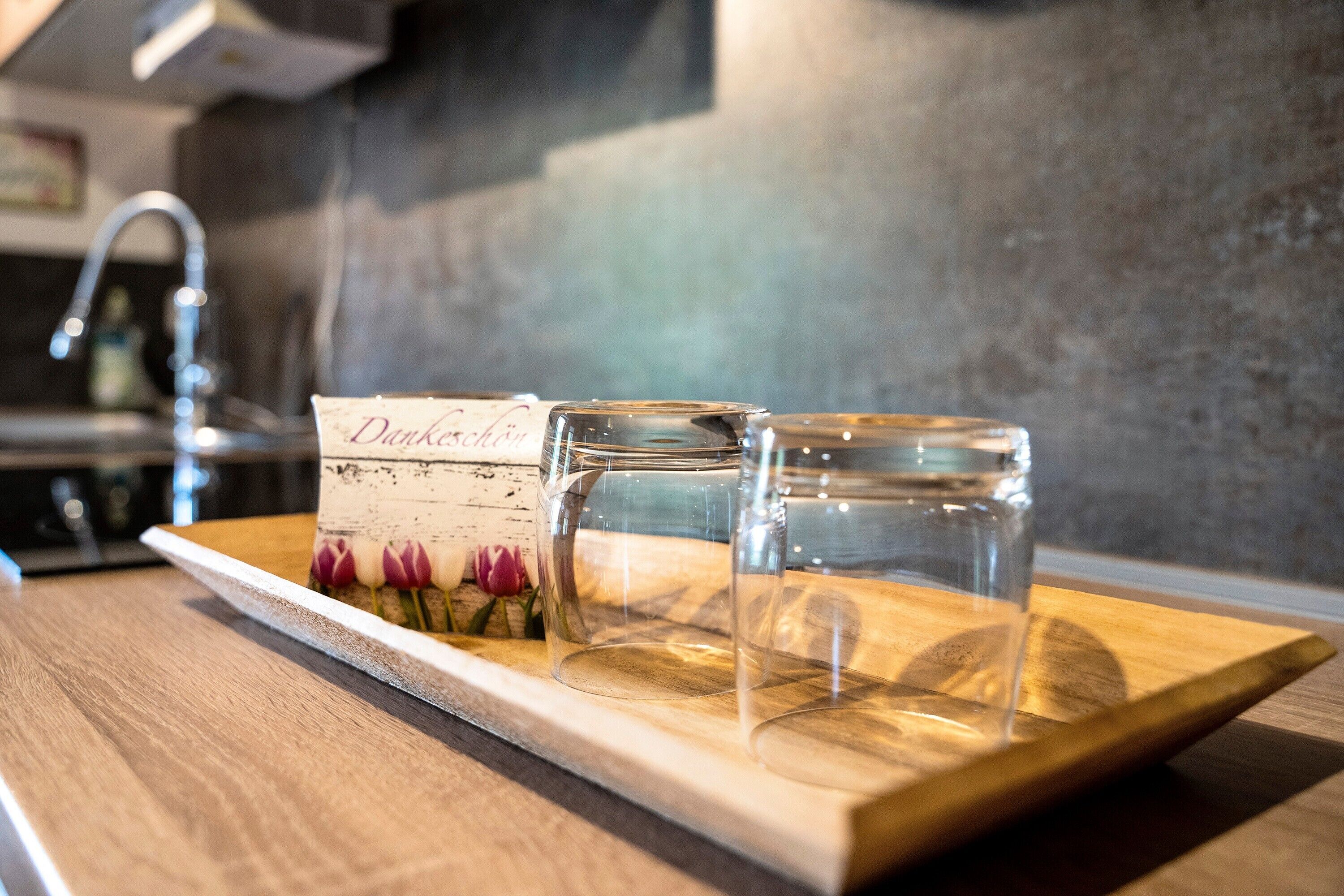 A wooden tray with two clear glasses and a card on a kitchen counter.