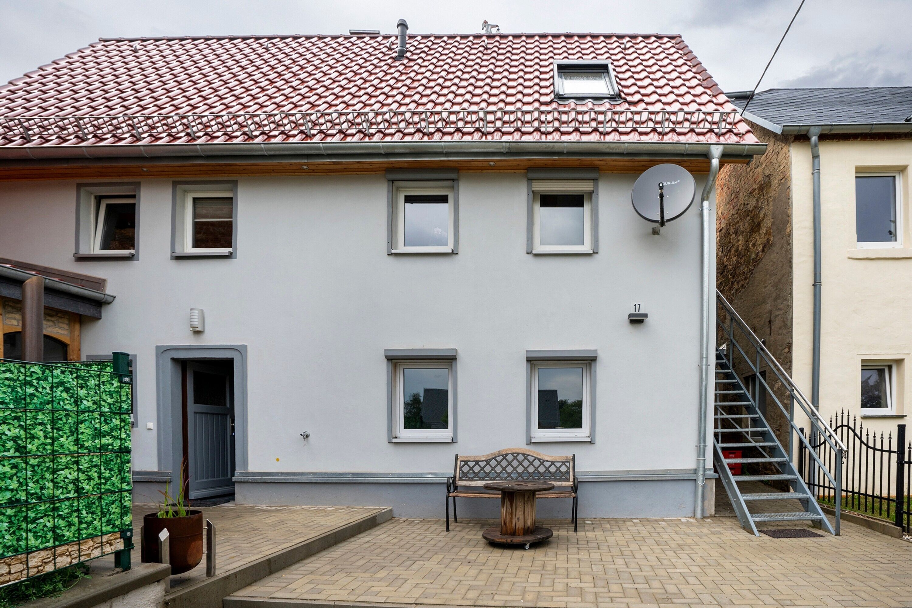A two-story building with a tiled roof, a satellite dish, and a staircase leading to the upper floor.